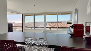 A modern kitchen with large windows, a dining table, and a red appliance. - Albufeira Modern Sea View Home 33 (Albufeira)