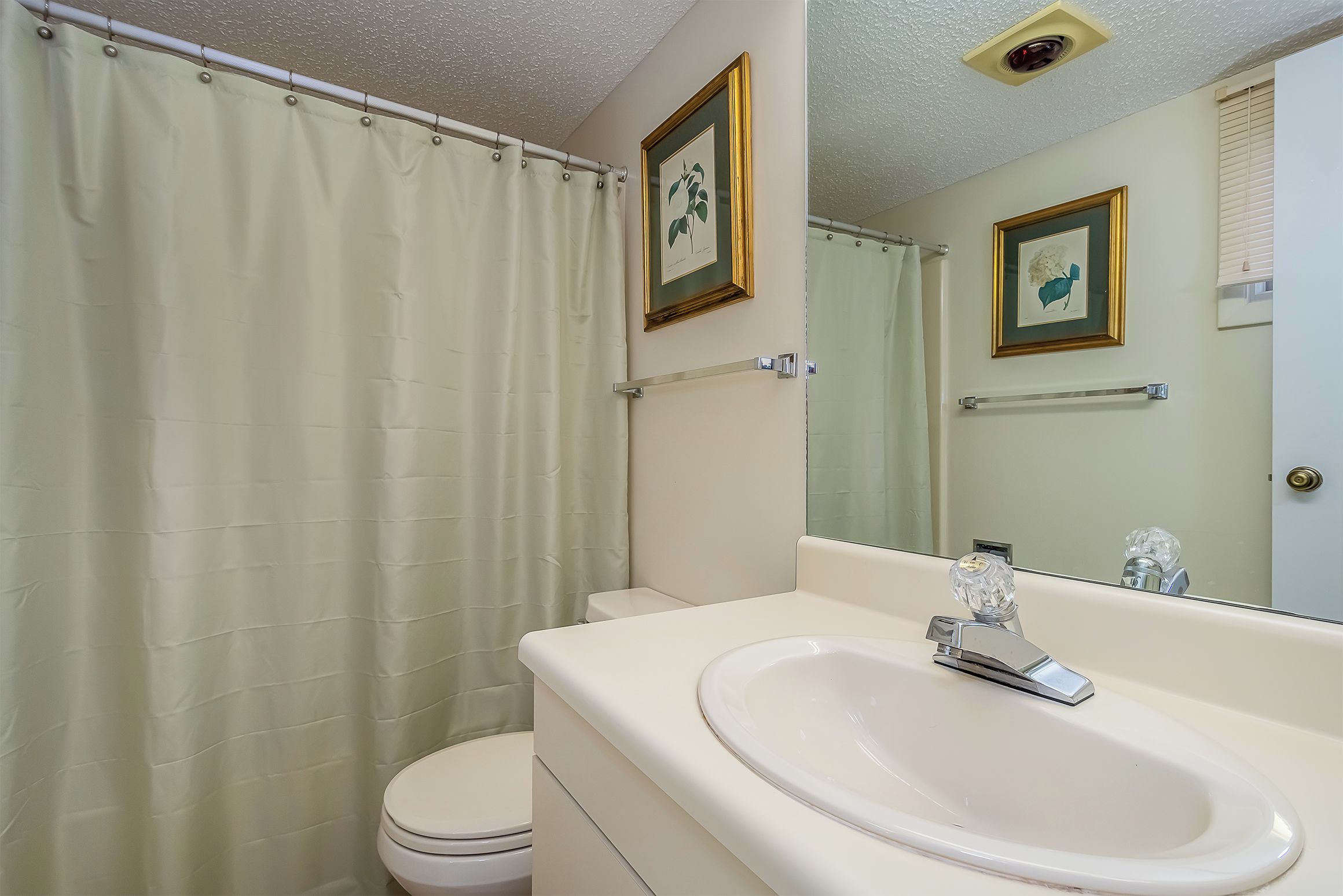 A bathroom with a toilet, a sink, a shower curtain, and framed artwork on the walls.