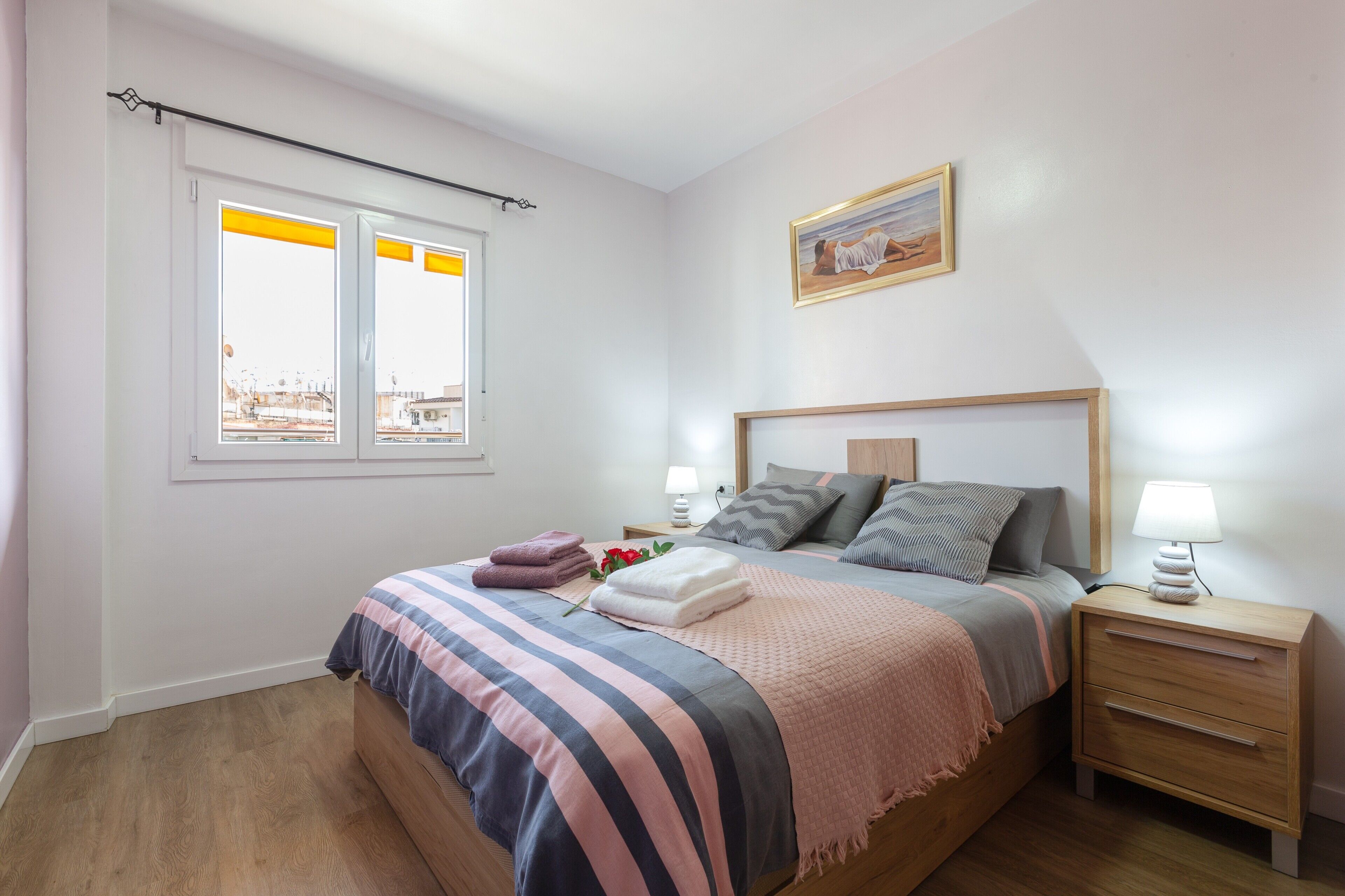 Un dormitorio con cama, mesitas de noche, una ventana y un cuadro en la pared.