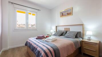 Un dormitorio con cama, mesitas de noche, una ventana y un cuadro en la pared.
