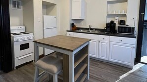 Una cocina compacta con armarios blancos, una mesa de madera y un horno empotrado.