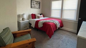 Un dormitorio con cama, mesita de noche, silla y ventana con persianas.