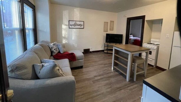 Un espacio habitable compacto con sofá, televisor, una pequeña mesa de comedor y kitchenette.