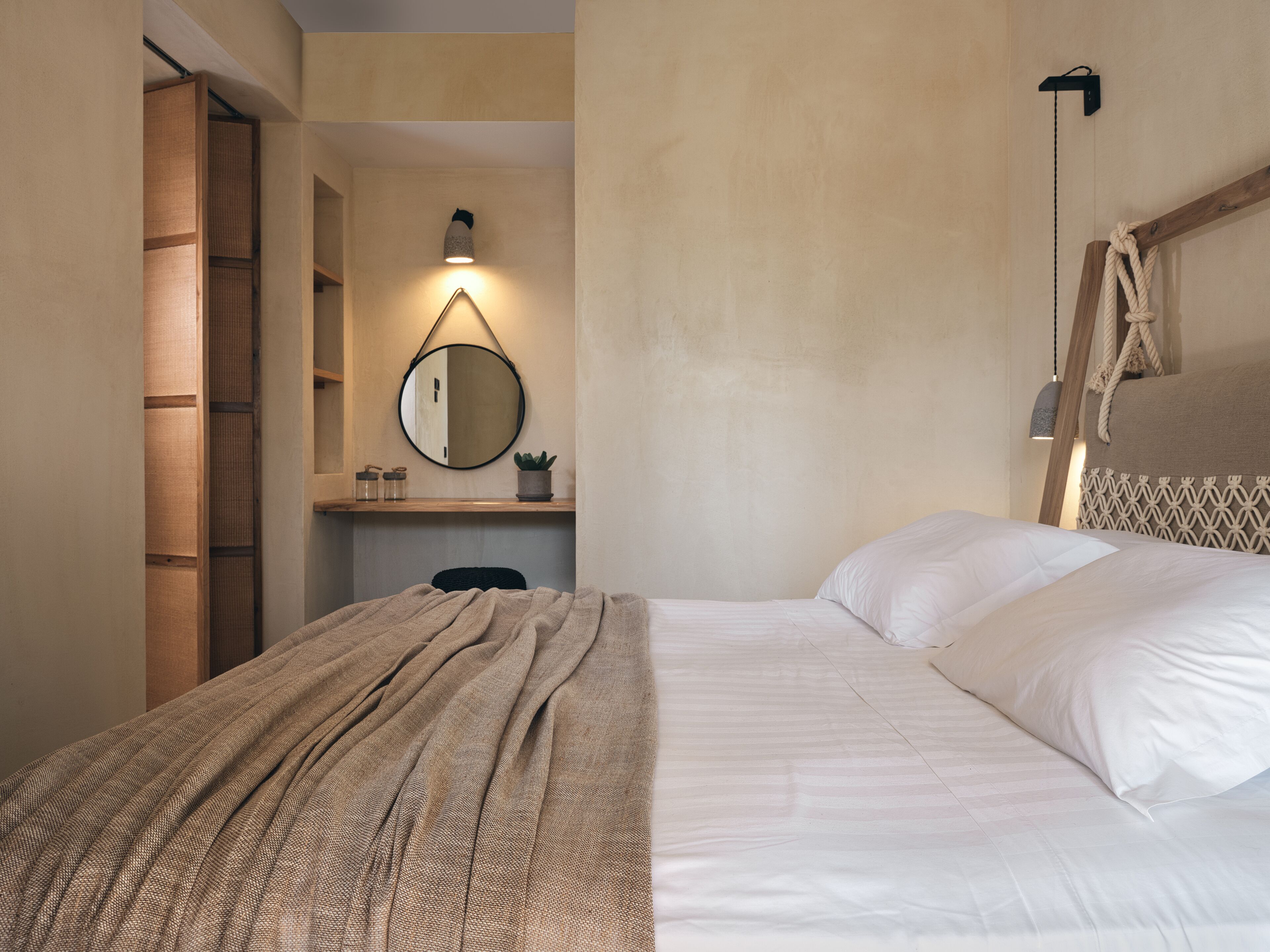 A bedroom with a bed, a bedside table, a mirror, and a hanging light fixture.