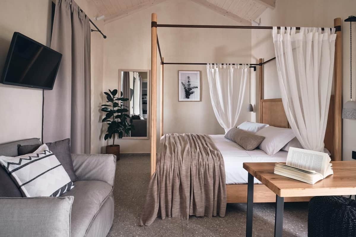 A bedroom with a four-poster bed, a bedside table with a book, a TV on the wall, and a plant.