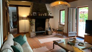 A cozy living room with a stone fireplace, a sofa, a wooden coffee table, and a wicker chair.