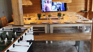 Ein Restaurant mit einer Tischfußballmaschine, einem an der Wand befestigten Fernseher und einem langen Esstisch, gedeckt für mehrere Gäste.