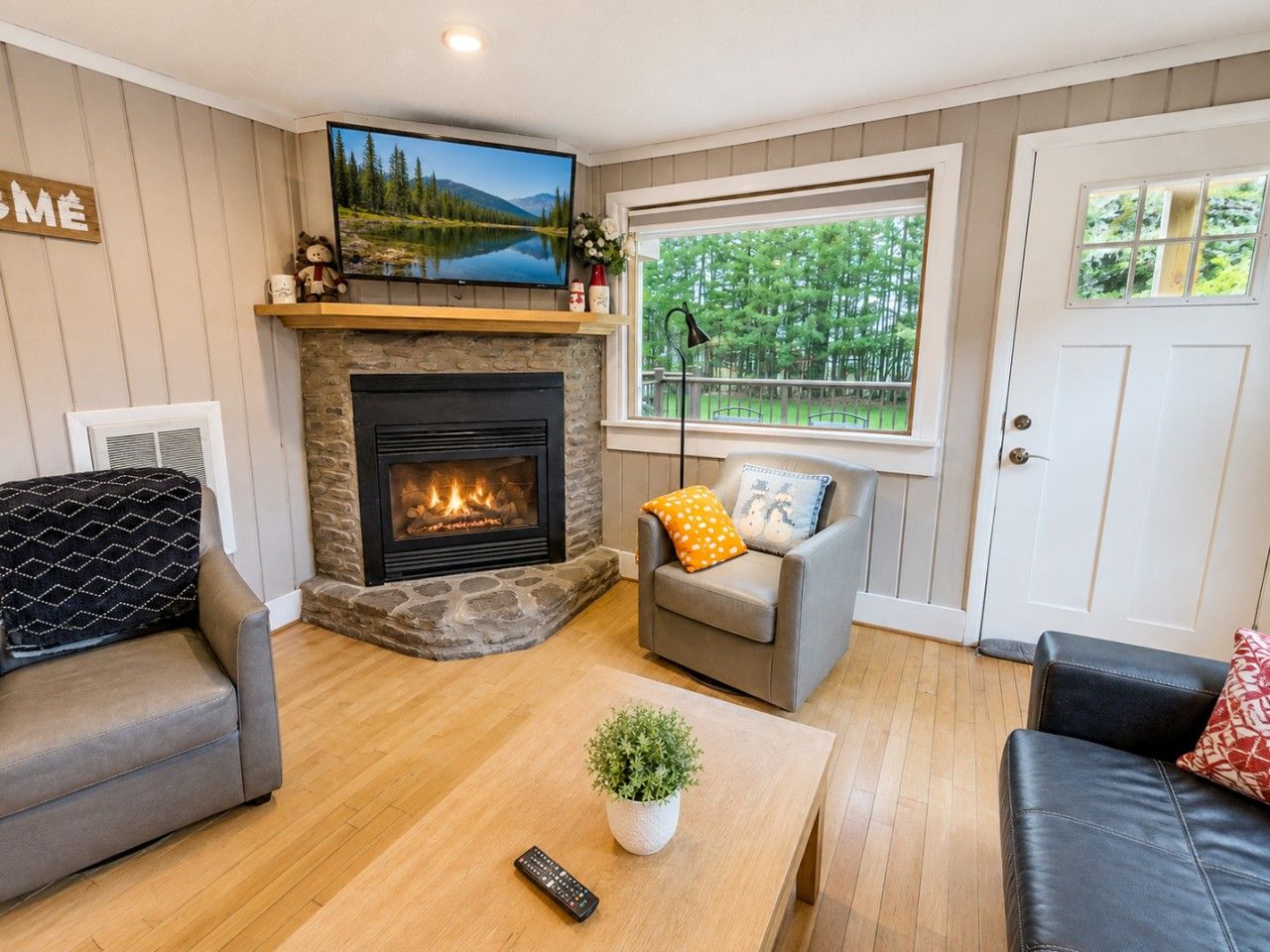 A cozy living room with a fireplace, a television mounted above it, and a large window offering a view of the outdoors.