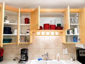 Cocina con alacenas de madera abiertas que contienen vajilla, vasos y utensilios de cocina.