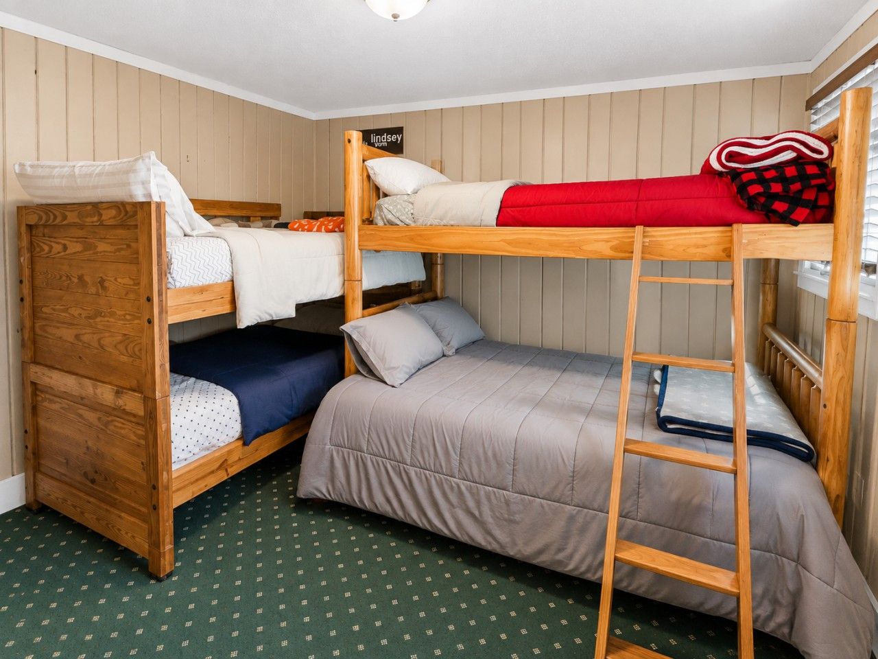A bunk bed room with a ladder, a wooden headboard, and a sign that reads 'lindsey'.