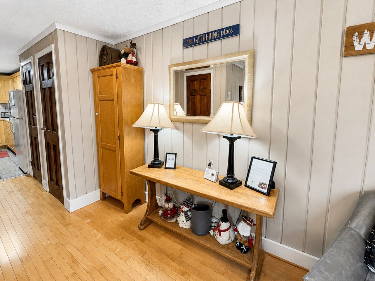 A hallway with a wooden bench, two wall-mounted lamps, a mirror, and a sign that reads 'the GATHERING place'.