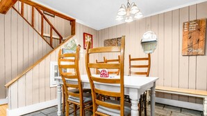 A dining area with wooden chairs, a white table, and a bench. There is a staircase with wooden railings and a chandelier. - Townhome Near Slopes Village Gated Parking Wi-Fi (Snowshoe)