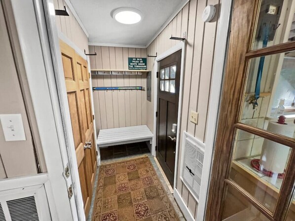 Un pasillo estrecho con un banco de madera, un cartel que prohíbe el uso de esquíes y botas de nieve, y una puerta de cristal que da a un baño.