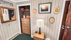 A room with a wooden dresser, a lamp, a framed picture, and a door with a sign above it. - Townhome Near Slopes Village Gated Parking Wi-Fi (Snowshoe)