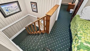 A room with a wooden staircase, a bed with a green and yellow patterned bedspread, and a small table with a lamp. - Townhome Near Slopes Village Gated Parking Wi-Fi (Snowshoe)