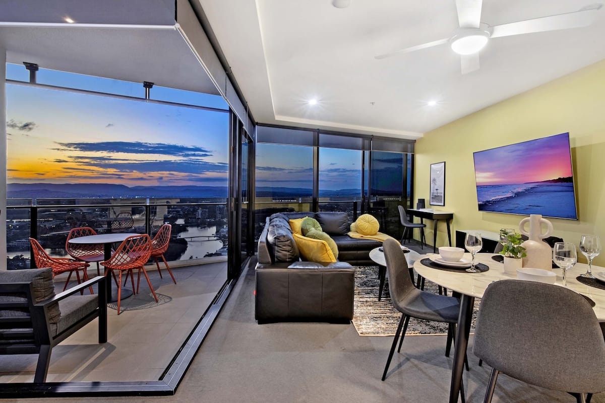 Una sala de estar moderna con vistas a la ciudad, un comedor con una mesa preparada para dos personas y una zona de estar acogedora con un sofá y sillones.