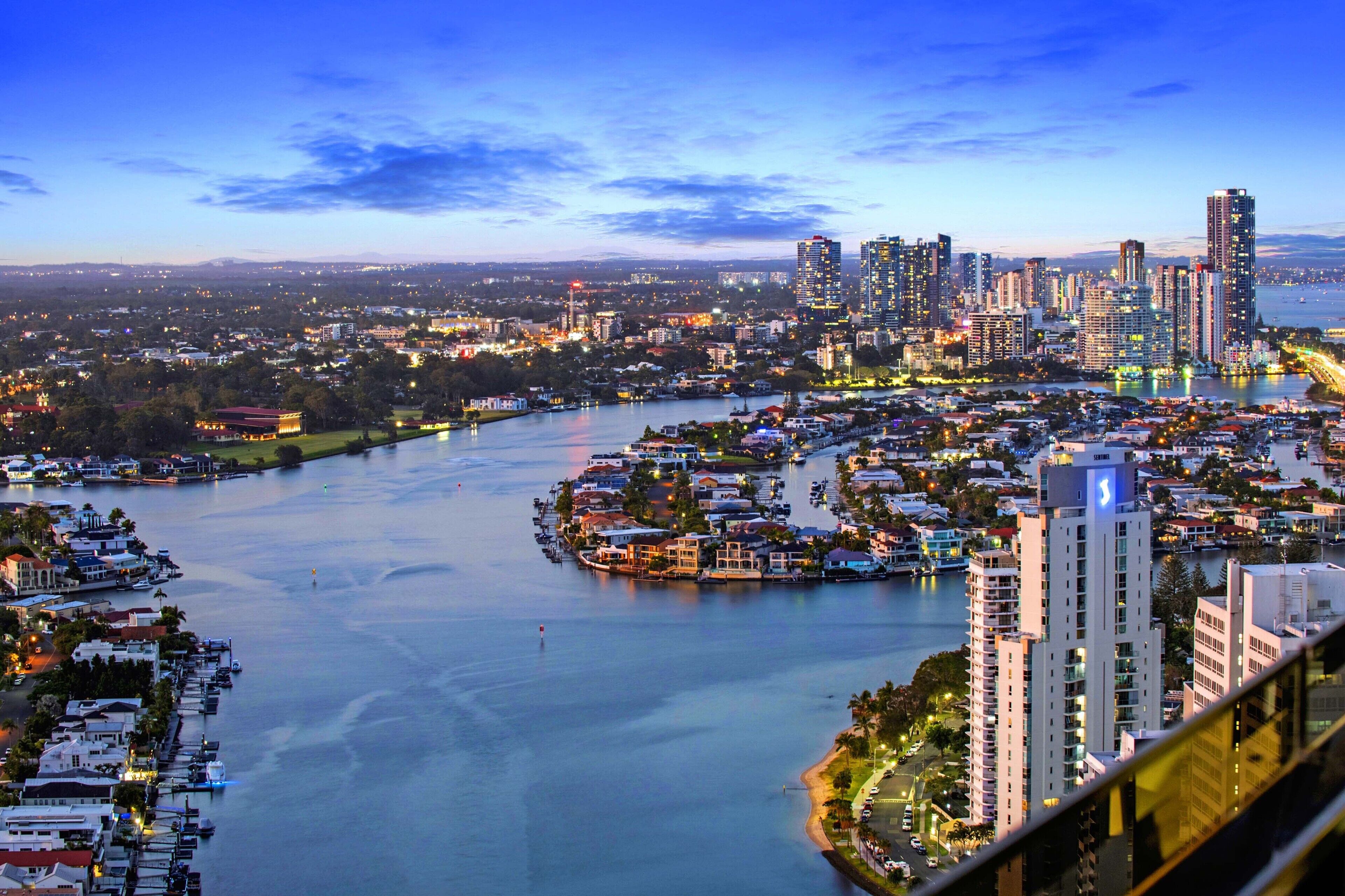 A coastal cityscape with a river, high-rise buildings, and a marina.