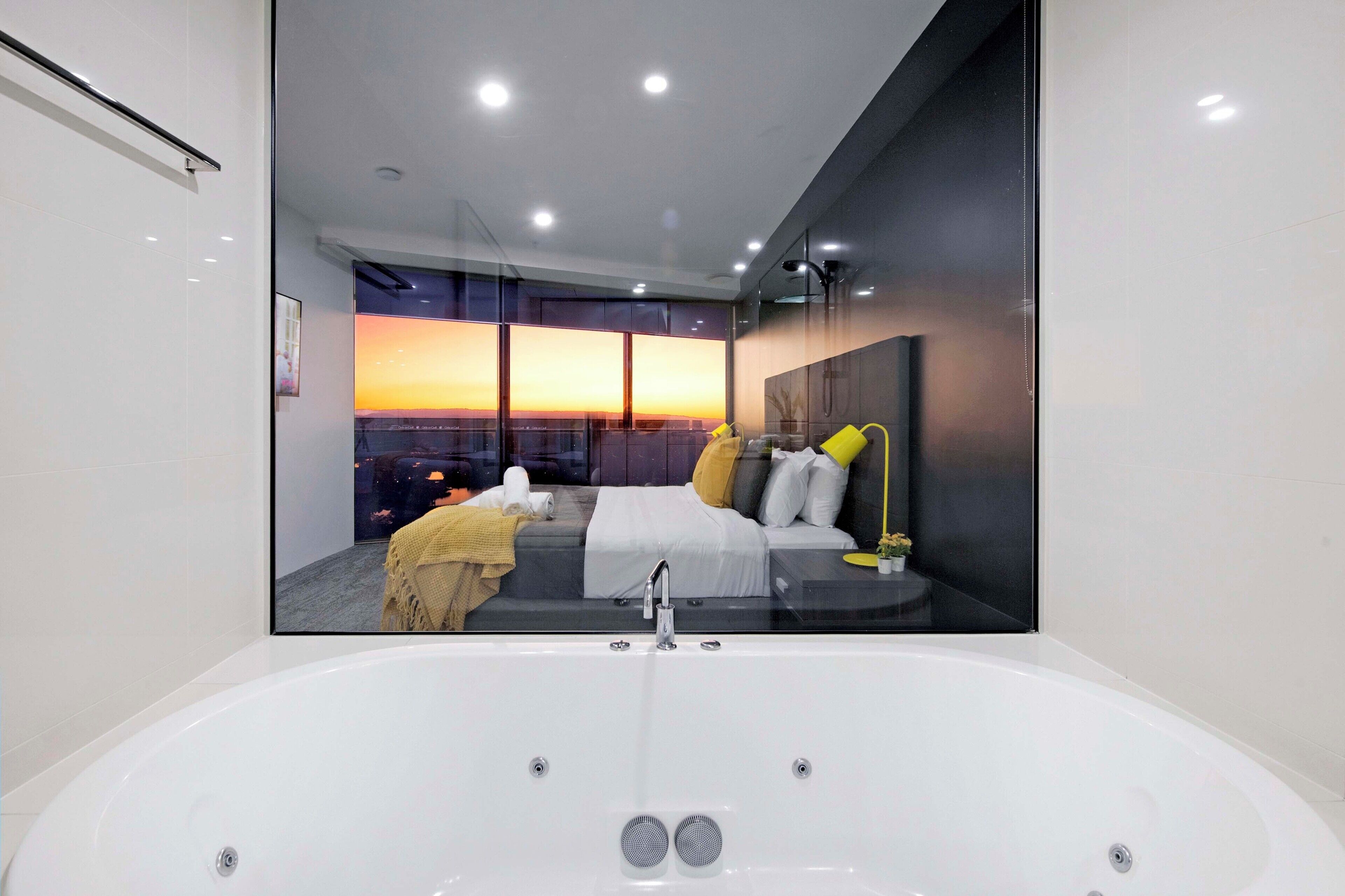 A modern bathroom with a large bathtub, a glass-enclosed shower area, and a view of a sunset through large windows.