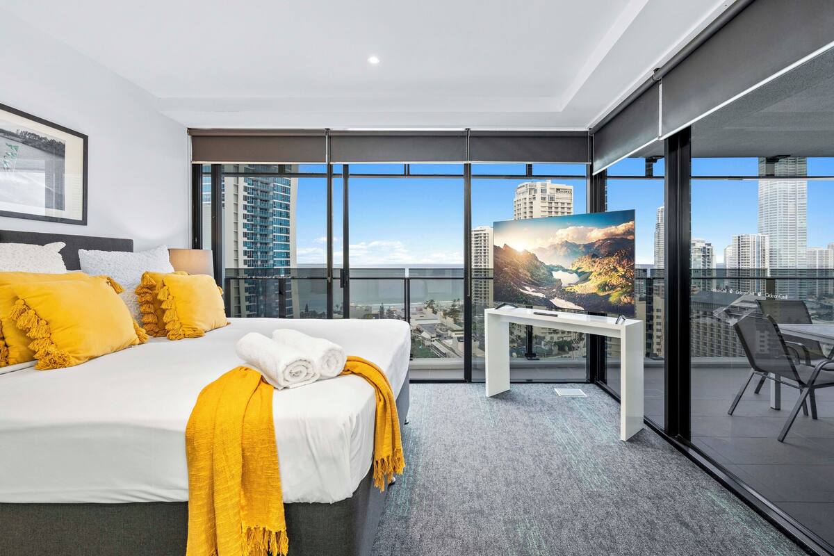 Habitación de hotel moderna con una cama grande, televisión y balcón con vistas a la ciudad.