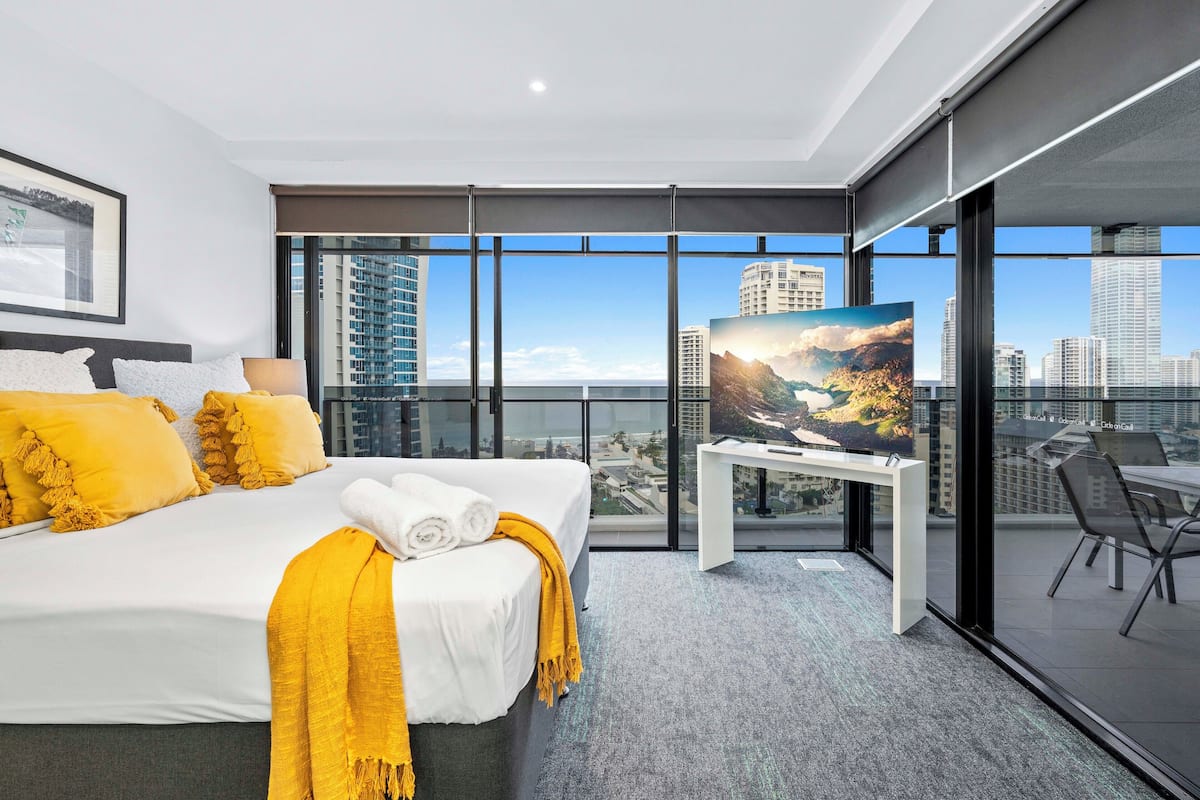 Habitación de hotel moderna con una cama grande, televisión y balcón con vistas a la ciudad.