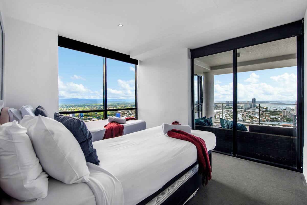 Una habitación de hotel moderna con una cama grande, dos ventanas, un balcón y vistas a la ciudad.