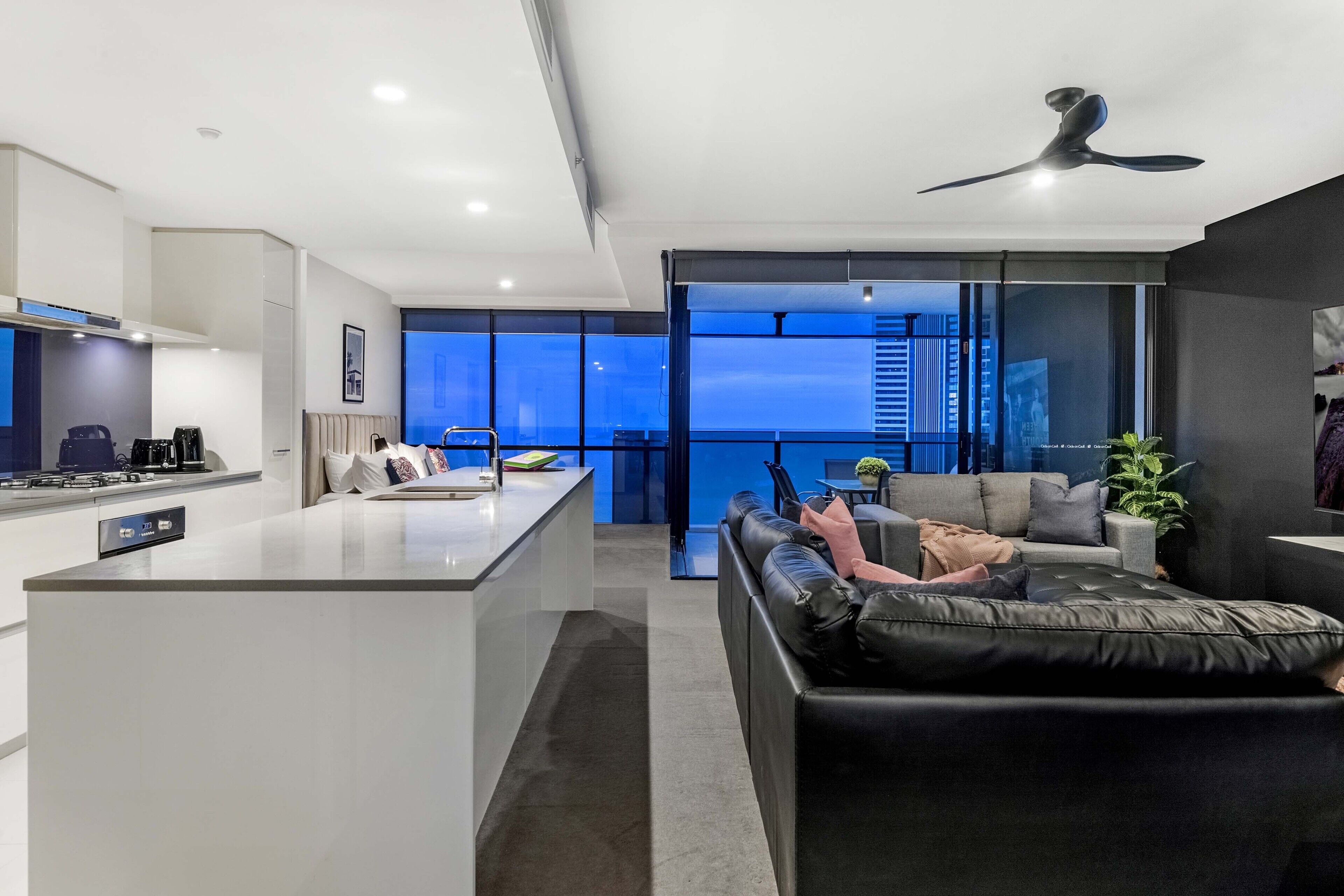 A modern living space with a kitchen, a sofa, and a balcony with a city view.