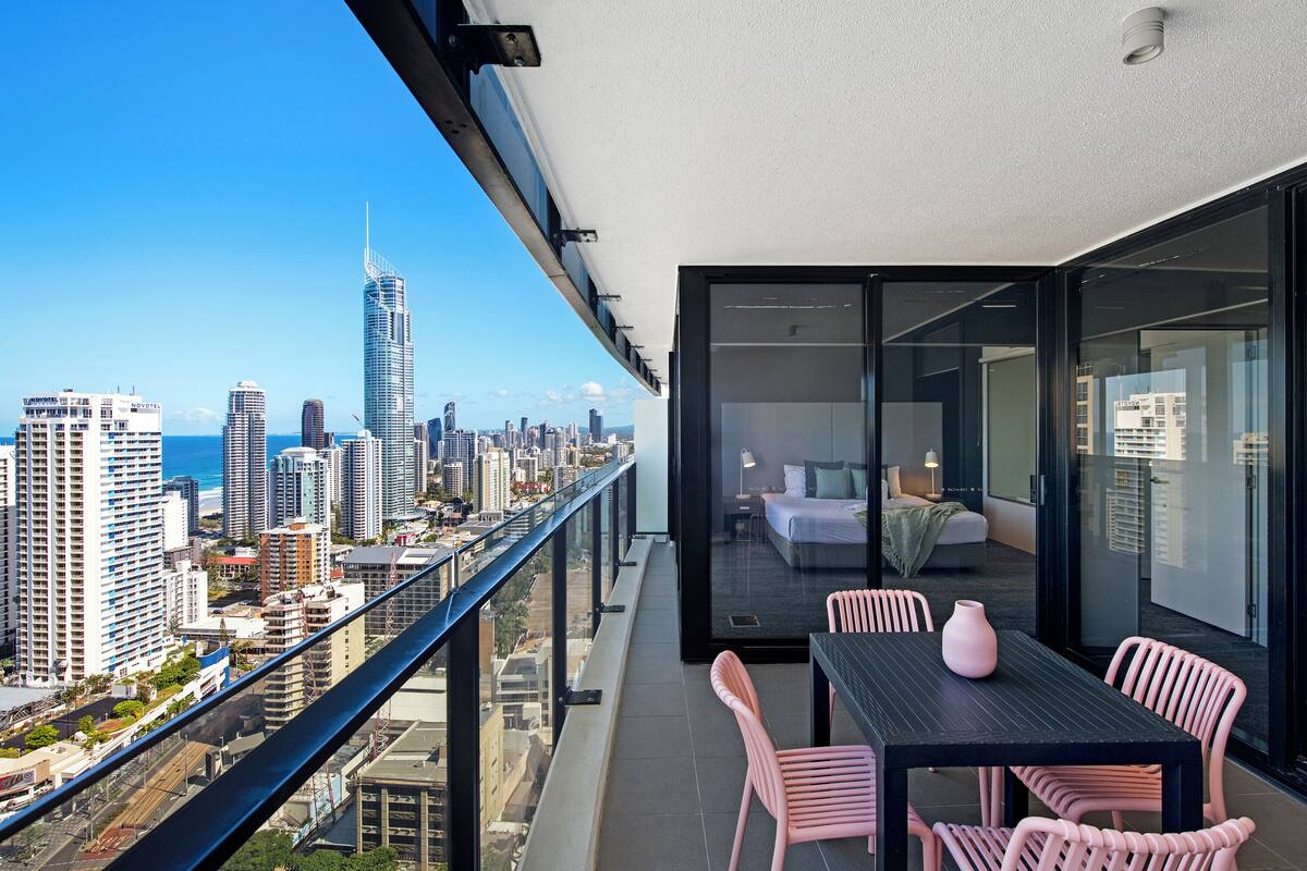 Un balcón con vista a la ciudad, una zona de comedor con sillas rosadas y un interior moderno.
