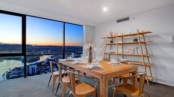 Comedor con vistas a un paisaje urbano y al río, que incluye una mesa de madera, sillas y un estante decorativo.