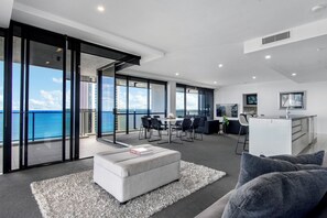A modern living room with a large window overlooking the sea, a dining area with chairs, a kitchen with a white countertop, and a sofa with a book on it. - Circle on Cavill - WOWSTAY (Surfers Paradise)