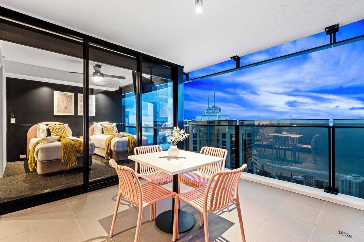 Una sala de estar moderna con una pared de vidrio, un comedor con mesa y sillas, y vista al horizonte de la ciudad.
