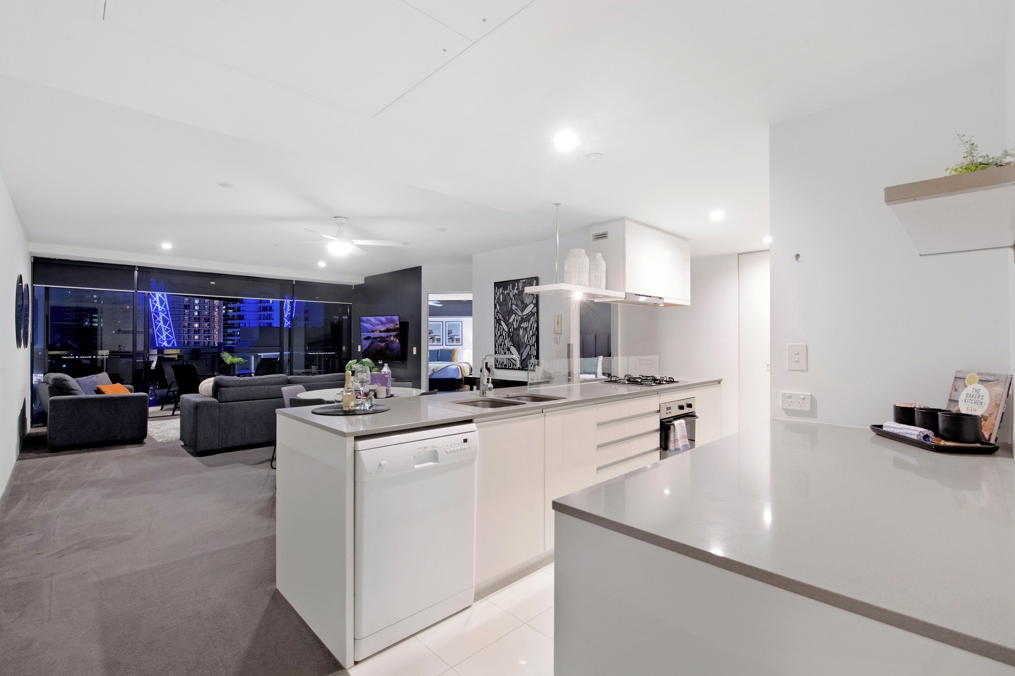 Cocina moderna con lavavajillas, una isla grande y zona de comedor con sofá y televisor.