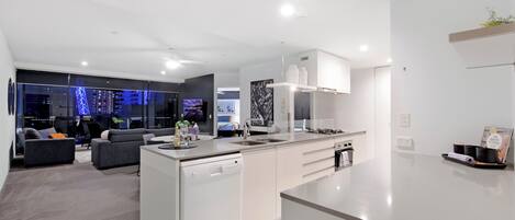 Cocina moderna con lavavajillas, una isla grande y zona de comedor con sofá y televisor.
