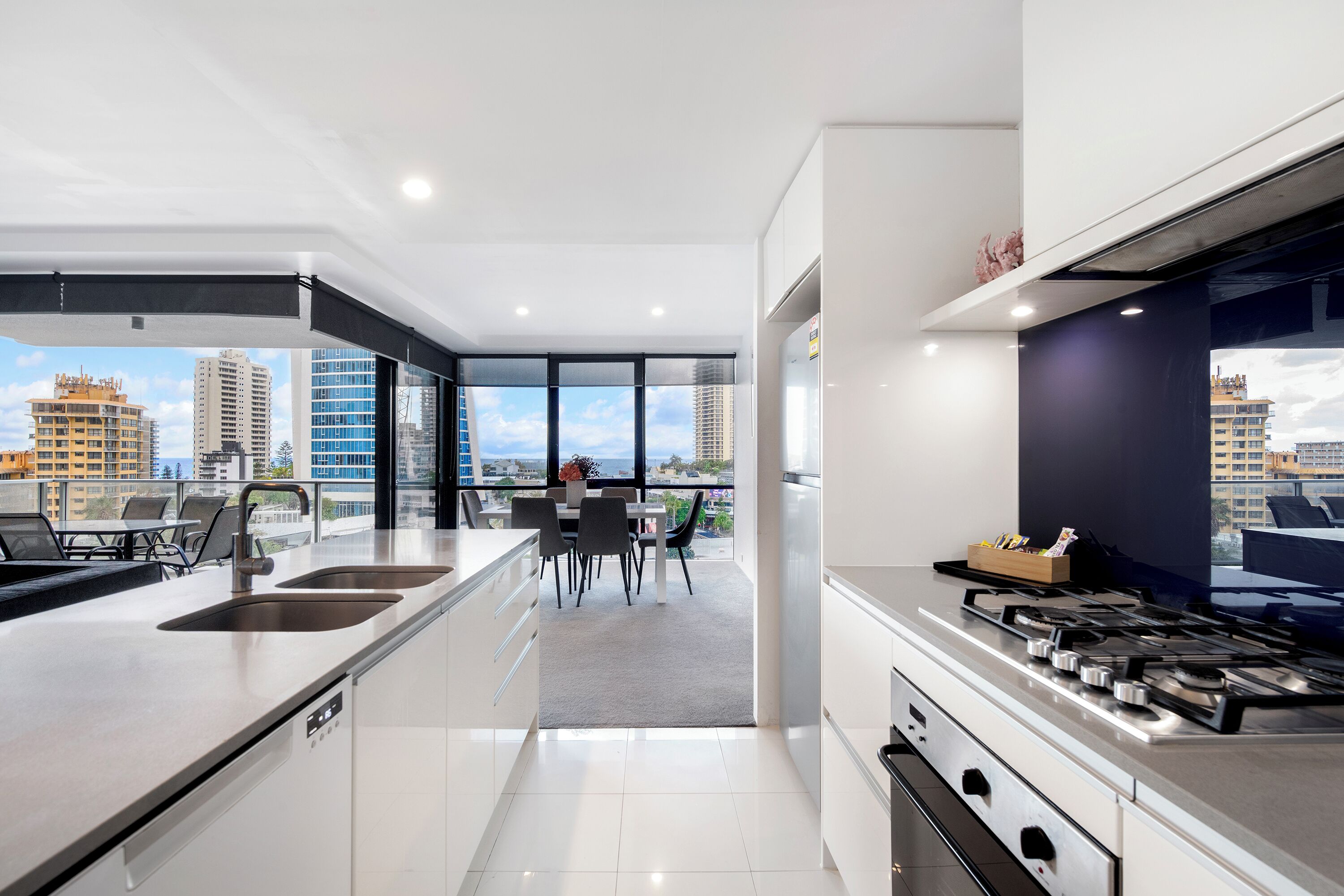 A modern kitchen with a central island, two sinks, and a dining area with a view of the city.
