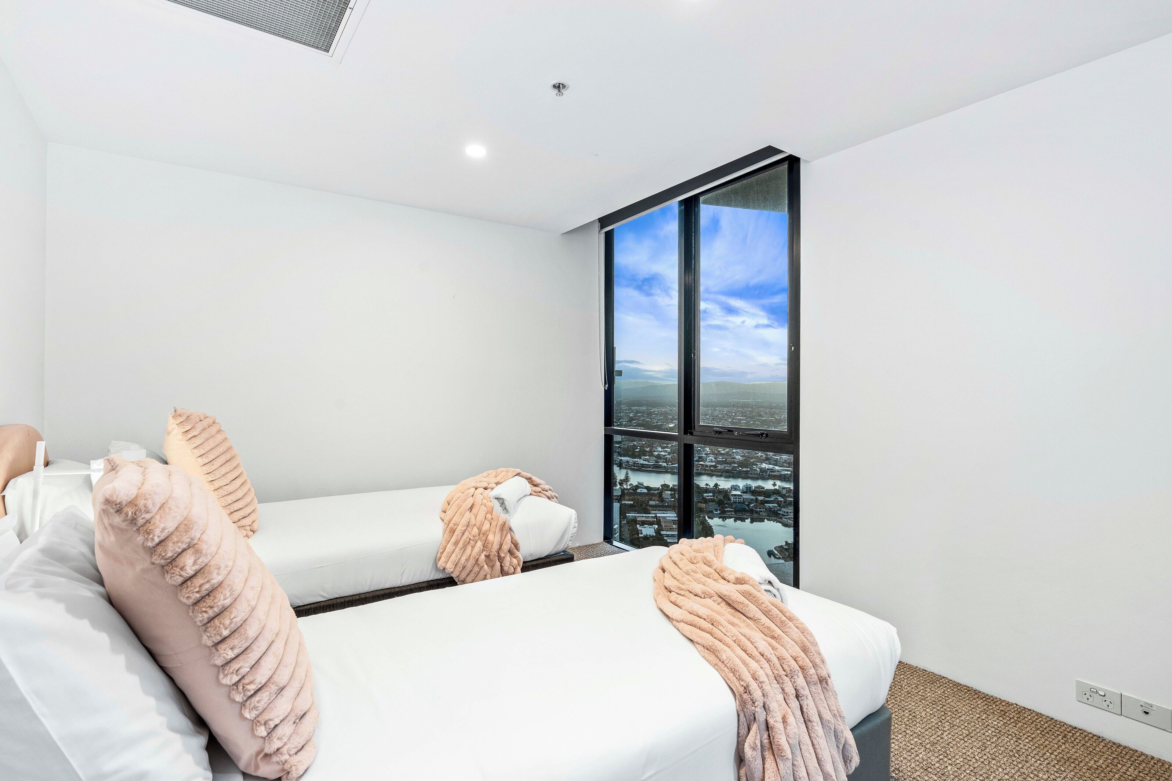Une chambre d’hôtel moderne avec deux lits, une grande fenêtre donnant sur la ville et un aménagement épuré et minimaliste.