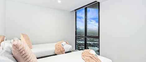 Une chambre d’hôtel moderne avec deux lits, une grande fenêtre donnant sur la ville et un aménagement épuré et minimaliste.