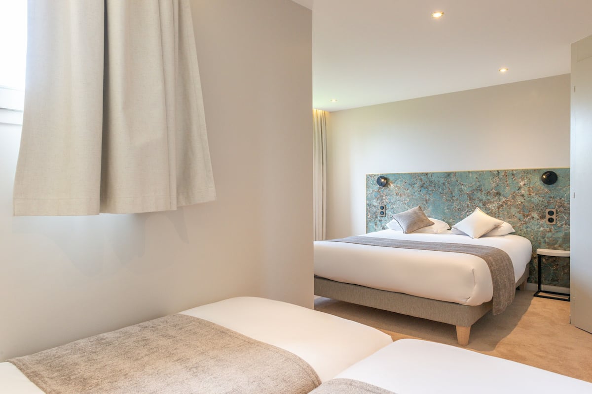 A modern bedroom with a large bed, a smaller bed, and a bedside table.