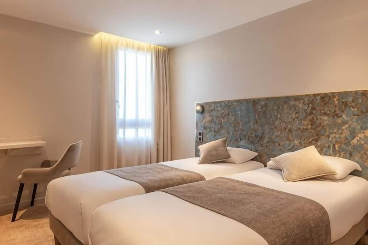 A hotel room with two beds, a desk, and a chair.