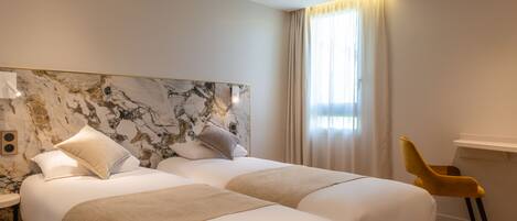 Habitación de hotel con dos camas, cabecera de mármol, una silla amarilla y un ventanal con cortinas.