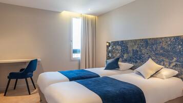 A hotel room with two beds, a desk, and a chair.