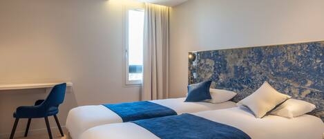 Ein Hotelzimmer mit zwei Betten, einem Schreibtisch und einem Stuhl.