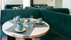 A dining area with teal upholstered booths, round tables with blue placemats, and a marble-topped table. - The Originals Boutique, Hôtel Porte de Dieppe (Saint-Aubin-sur-Scie)