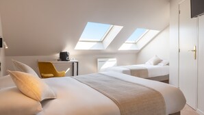 Habitación de hotel con dos camas, un escritorio, una silla y tragaluces.