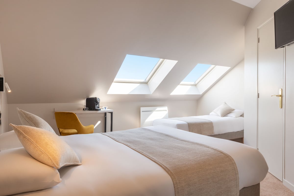 A hotel room with two beds, a desk, a chair, and skylights.