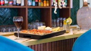 A bar area with a glass of red wine, a tray of cured meats, and a bottle of lemon. - The Originals Boutique, Hôtel Porte de Dieppe (Saint-Aubin-sur-Scie)