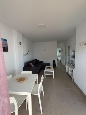 A modern living room with a sofa, a dining table with chairs, and a TV stand.