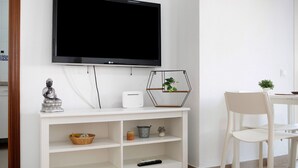 Un meuble blanc pour la télévision, sur lequel est posée une télévision à écran plat, ainsi qu’une statue, un panier et une télécommande.