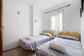 Ein Schlafzimmer mit zwei Betten, einem Fenster mit Vorhängen und einer Tür.