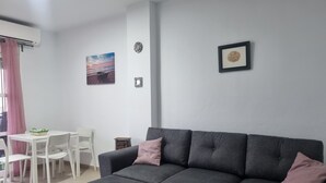 Un salon avec un canapé gris, une petite table, des chaises blanches et un tableau encadré au mur.