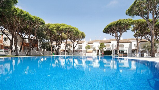 Une piscine d’un bleu éclatant, entourée d  ’arbres et bordée de bâtiments blancs dotés de balcons.