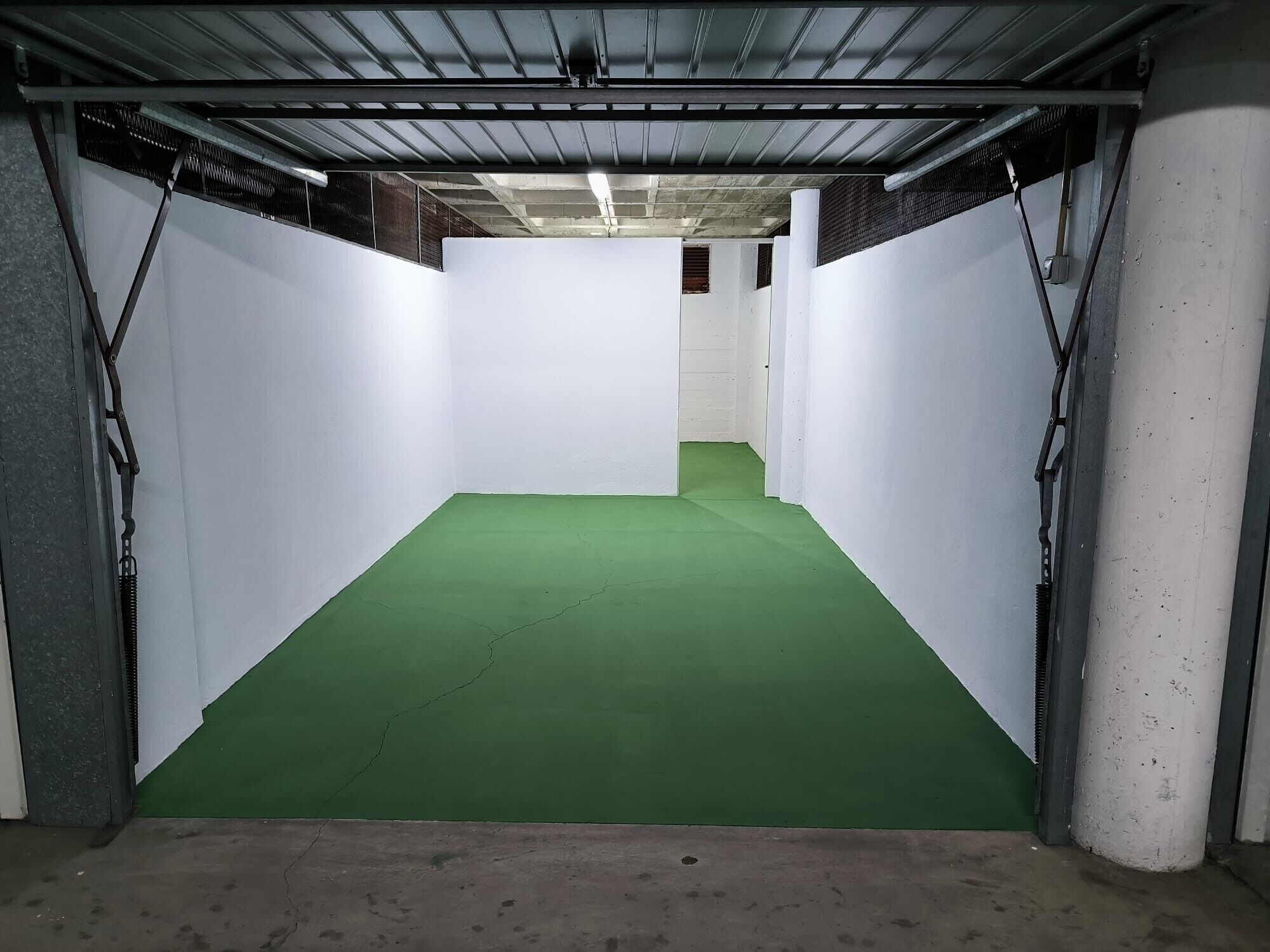 A room with white walls, a green floor, and metal beams on the ceiling.